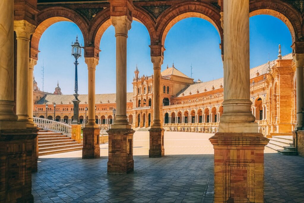 Historic Plaza de España in Seville, Spain, viewed through ornate arches surrounding its grand tiled courtyard