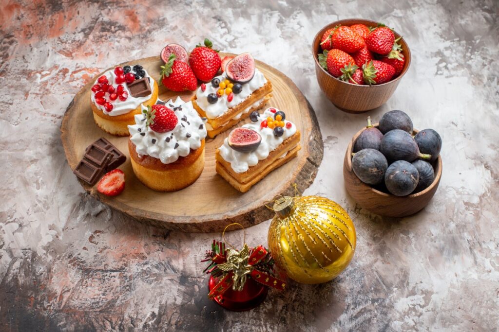 Festive dessert board with strawberries, figs, blueberries, cream pastries, chocolate, and a golden Christmas ornament