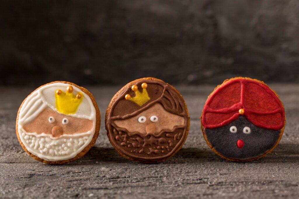 Three decorated biscuits show a bearded Santa, a crowned chocolate figure, and a red-hatted dark-faced character.