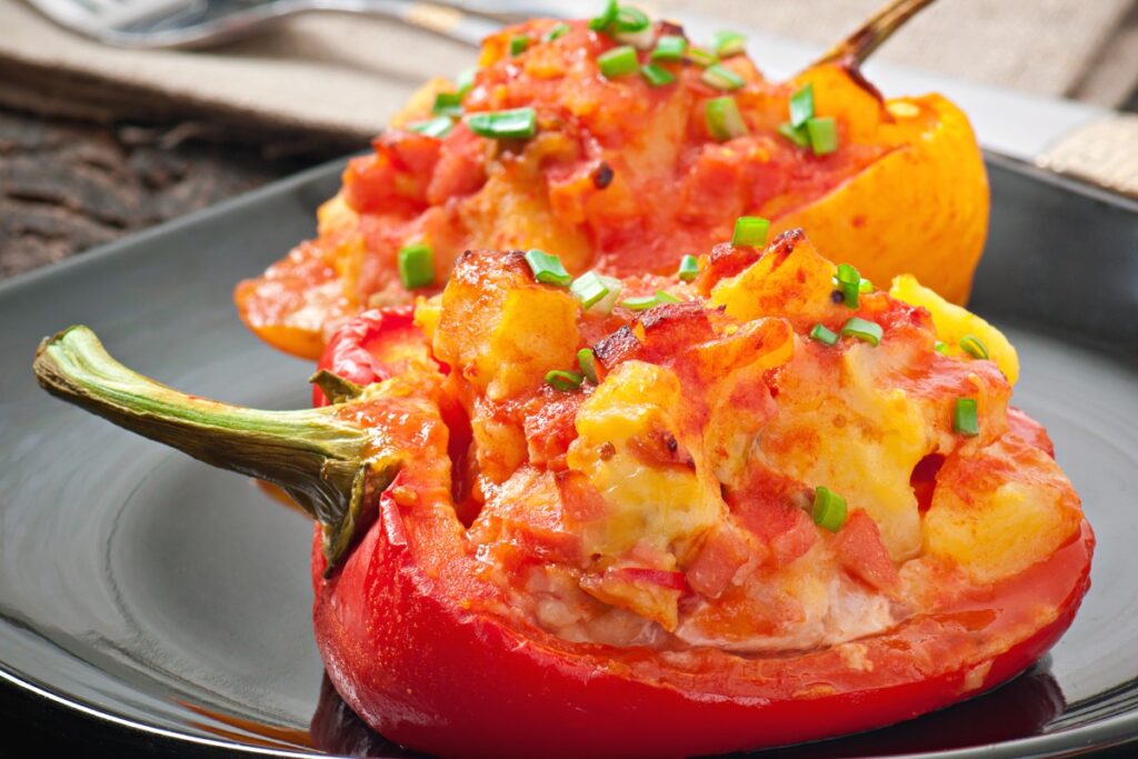 Gevulde rode en gele paprika’s met aardappelen, chorizo, tomatensaus en gesmolten kaas op een zwart bord