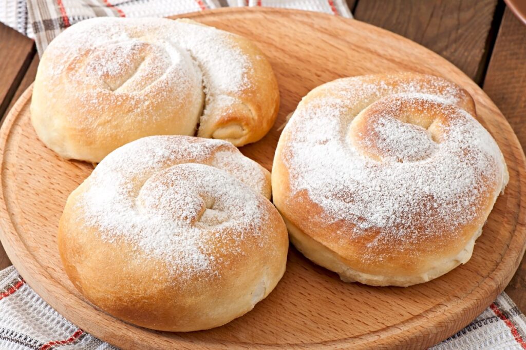 Three powdered ensaimadas rest on a round wooden board, with their golden spiral pastries clearly visible.