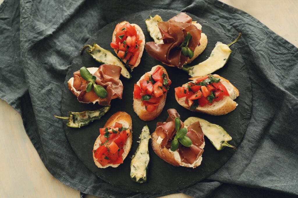 Savoury Spanish tapas with tomato, prosciutto and vegetables arranged on a dark serving board beside the lorem ipsum post.