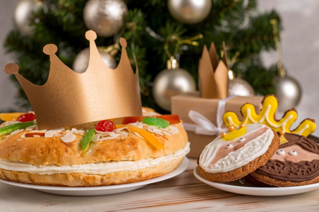 Festive ring cake and decorated biscuits with a gold crown beneath Christmas tree ornaments and gift boxes