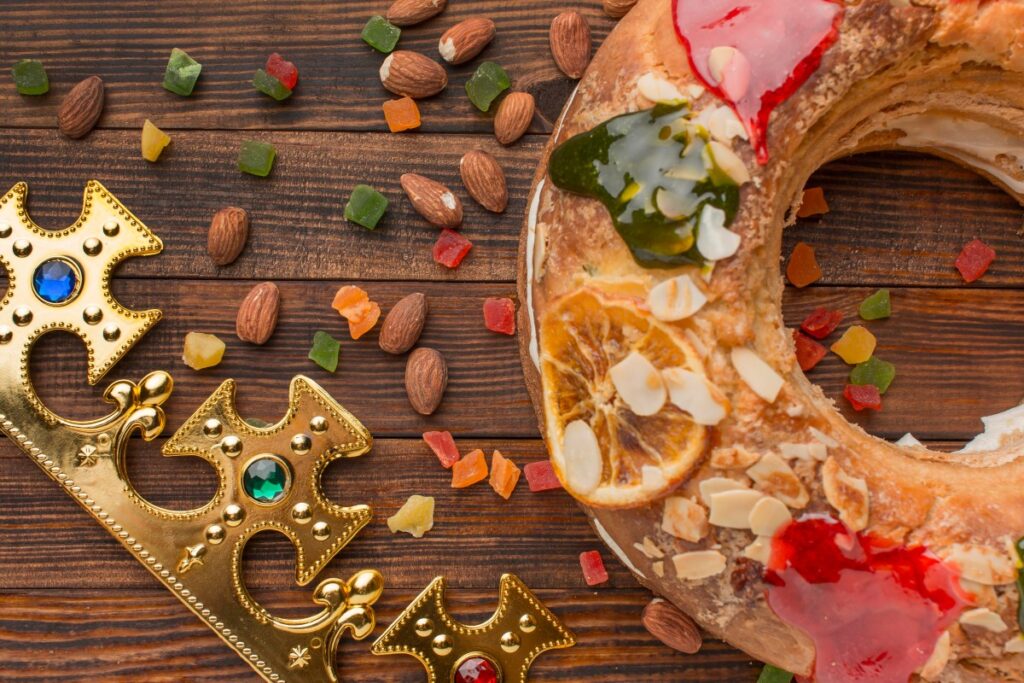 A festive Roscón de Reyes ring cake with almonds, candied fruit and ornate gold crowns on a wooden table